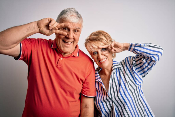 Älteres schönes Paar, das zusammen vor isoliertem weißem Hintergrund steht, Friedenssymbol mit den Fingern über dem Gesicht, fröhlich lächelnd den Sieg zeigend - Foto, Bild
