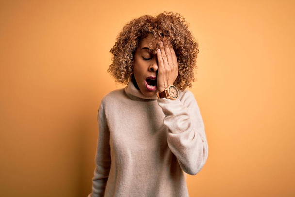 Young beautiful african american woman wearing turtleneck sweater over yellow background Yawning tired covering half face, eye and mouth with hand. Face hurts in pain. - Photo, Image