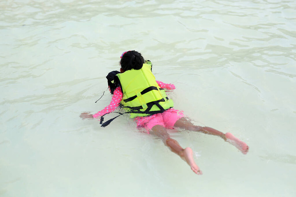 Parte posterior de la niña asiática nadar en la piscina al aire libre y usar chaleco salvavidas
 - Foto, Imagen