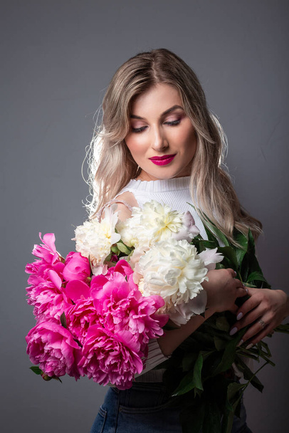 Skin care concept. Photo of blonde girl with pink peonies on grey background. - Fotografie, Obrázek