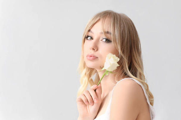 Beautiful young woman with rose on light background - Photo, Image