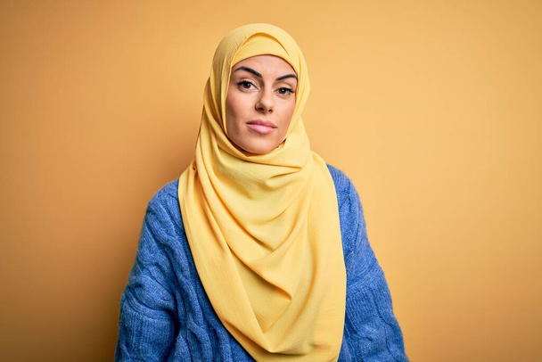 Junge schöne brünette Muslimin trägt arabischen Hijab über isoliertem gelben Hintergrund und sieht schläfrig und müde aus, erschöpft von Müdigkeit und Kater, faule Augen am Morgen. - Foto, Bild