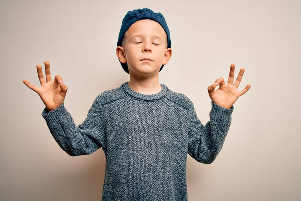 Young little caucasian kid with blue eyes wearing wool cap over isolated background relax and smiling with eyes closed doing meditation gesture with fingers. Yoga concept. - Photo, Image