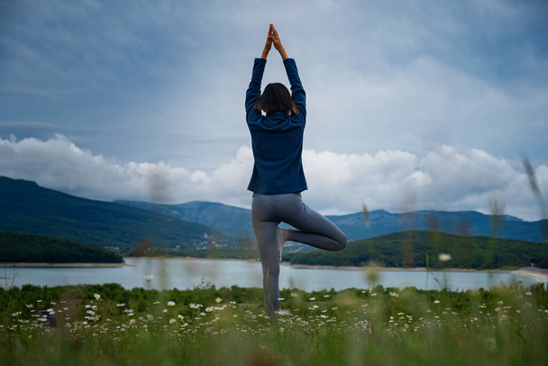 Uma jovem mulher fazendo Hatha ioga no campo de pé em pose de árvore de ioga ou asana Vrikshasana tre pose. Harmonia com a natureza, o conceito de saúde e fitness. Auto-análise e busca de alma vista traseira
 - Foto, Imagem