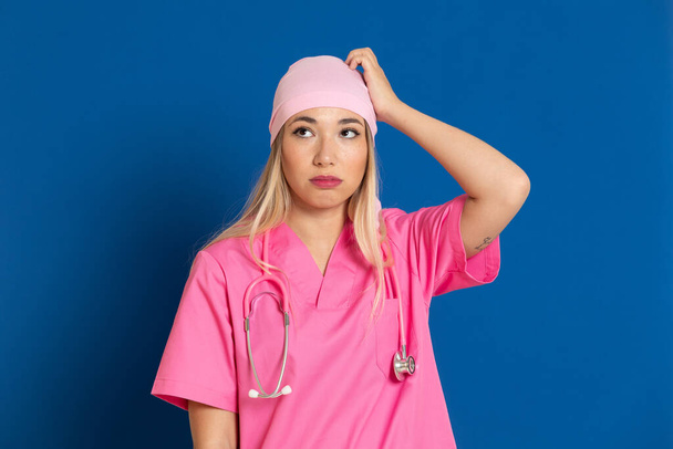Jonge arts met een roze uniform en sjaal op een blauwe achtergrond - Foto, afbeelding