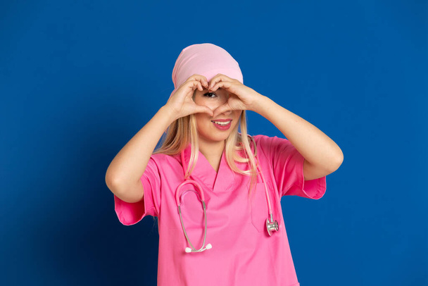 Jonge arts met een roze uniform en sjaal op een blauwe achtergrond - Foto, afbeelding