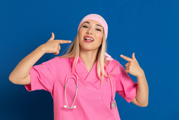 Young doctor with a pink uniform and a scarf on a blue background - Photo, Image