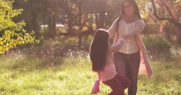 Mom spinning with daughter holding hands together at autumn park among trees with a fairytale color. Tinted footage. Copy space. Concept family. Prores 422 - Кадры, видео