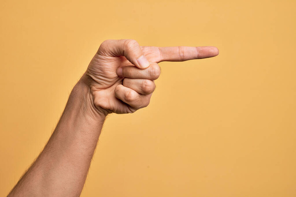 Mano de joven caucásico mostrando los dedos sobre fondo amarillo aislado apuntando con el dedo índice hacia un lado, sugiriendo y seleccionando una opción - Foto, imagen