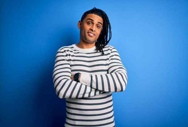Joven hombre afro afroamericano guapo con rastas que usan suéter a rayas casual cara feliz sonriendo con los brazos cruzados mirando a la cámara. Persona positiva
. - Foto, imagen