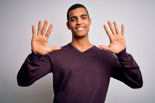 Junge gutaussehende afrikanisch-amerikanische Mann trägt lässigen Pullover über weißem Hintergrund zeigt und zeigt mit den Fingern Nummer zehn und lächelt zuversichtlich und glücklich. - Foto, Bild