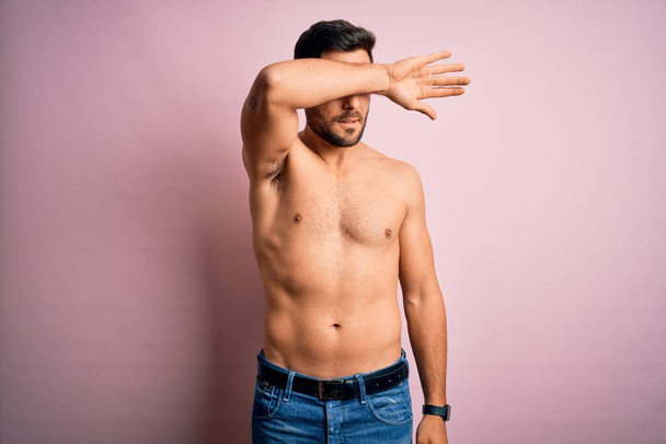 Young handsome strong man with beard shirtless standing over isolated pink background covering eyes with arm, looking serious and sad. Sightless, hiding and rejection concept - Photo, Image