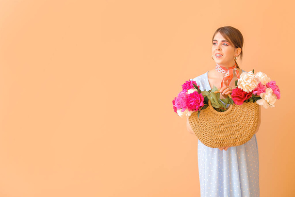 Young woman with beautiful peony flowers in bag on color background - Foto, Imagen