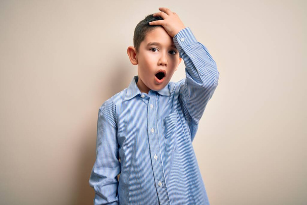 Young little boy kid wearing elegant shirt standing over isolated background surprised with hand on head for mistake, remember error. Forgot, bad memory concept. - Photo, Image