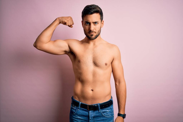 Nuori komea vahva mies parta paidaton seisoo yli eristetty vaaleanpunainen tausta Vahva henkilö osoittaa käsivarren lihas, luottavainen ja ylpeä vallasta - Valokuva, kuva