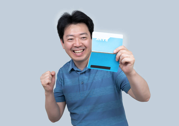 Asijský muž středního věku držící v ruce bankovní vkladní knížku na šedém pozadí. - Fotografie, Obrázek