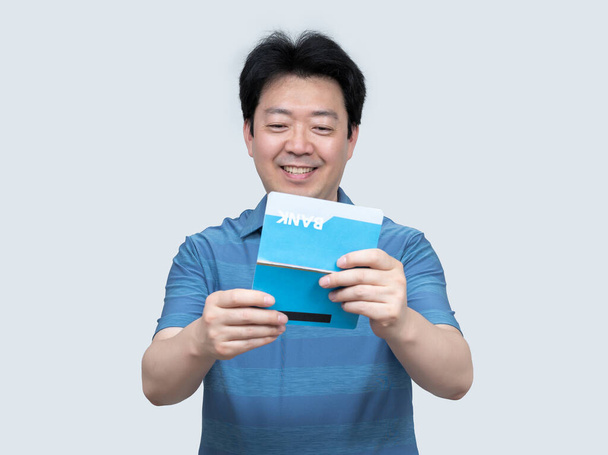 Un asiático de mediana edad sosteniendo una libreta bancaria en su mano sobre un fondo gris
. - Foto, imagen