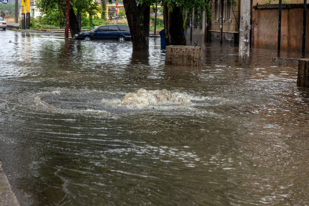 rijdende auto op overstroomde weg tijdens overstromingen veroorzaakt door hevige regenval. Auto 's drijven op water, overstroomde straten. Splash op de auto. Overstroomde stadsweg met grote plas. Overstromingen na hevige regenval in de stad - Foto, afbeelding