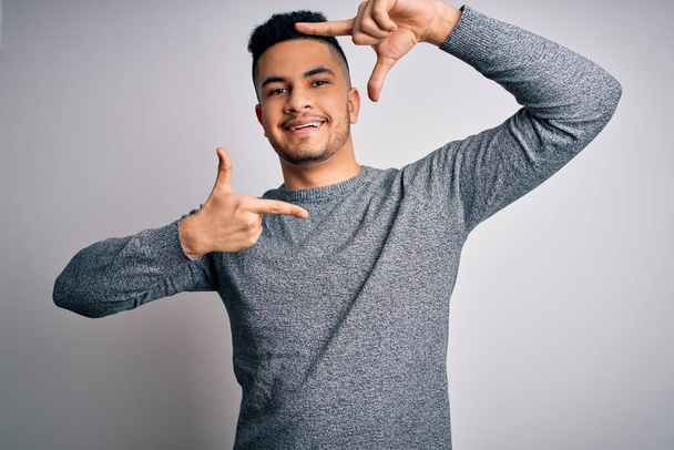 Young handsome man wearing casual sweater standing over isolated white background smiling making frame with hands and fingers with happy face. Creativity and photography concept. - Fotoğraf, Görsel