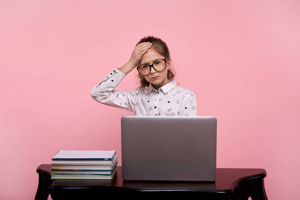 surprised young girl sits at a laptop in a white shirt and black-rimmed glasses - Фото, изображение