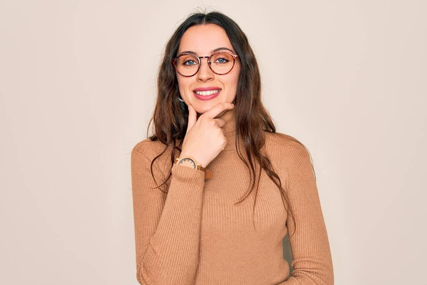 Young beautiful woman wearing casual turtleneck sweater and glasses over white background looking confident at the camera smiling with crossed arms and hand raised on chin. Thinking positive. - Fotoğraf, Görsel