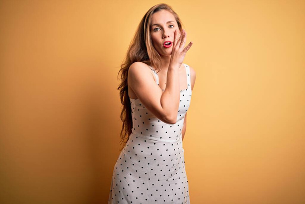 Young beautiful blonde woman on vacation wearing summer dress over yellow background hand on mouth telling secret rumor, whispering malicious talk conversation - Foto, Imagen