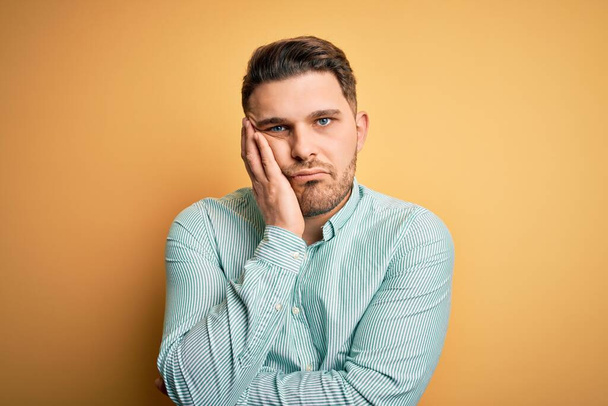 Young business man with blue eyes wearing elegant green shirt over yellow background thinking looking tired and bored with depression problems with crossed arms. - Photo, Image
