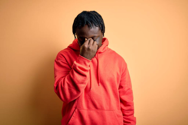 Junge afrikanisch-amerikanische sportliche Mann trägt Sweatshirt mit Kapuzenpulli über gelbem Hintergrund müde reiben Nase und Augen Gefühl von Müdigkeit und Kopfschmerzen. Konzept für Stress und Frustration. - Foto, Bild