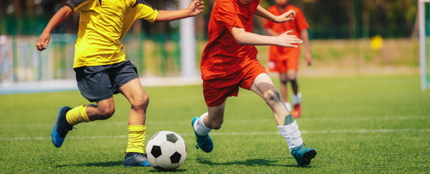 Urheilulliset jalkapallopojat juoksevat pallon perässä kaksintaistelussa. Koulun jalkapallokilpailu kahden junioritason pelaajan välillä. Monikansalliset lapset pelata urheilua - Valokuva, kuva