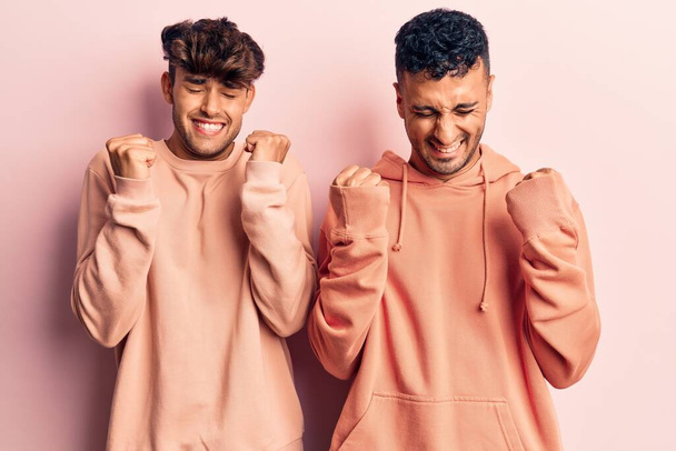 Young gay couple wearing casual clothes excited for success with arms raised and eyes closed celebrating victory smiling. winner concept.  - Fotoğraf, Görsel
