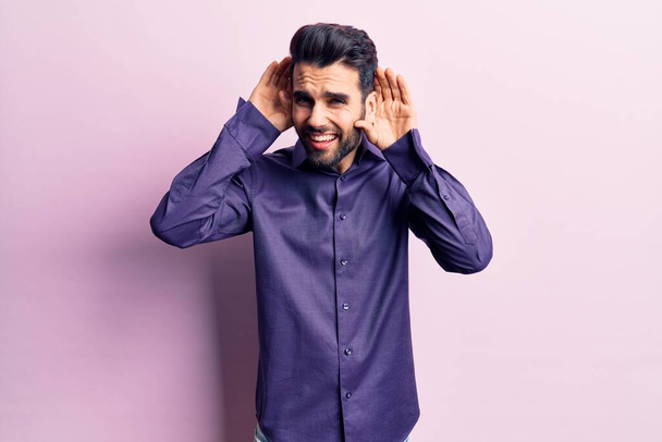 Young handsome man with beard wearing casual shirt trying to hear both hands on ear gesture, curious for gossip. hearing problem, deaf  - Photo, Image