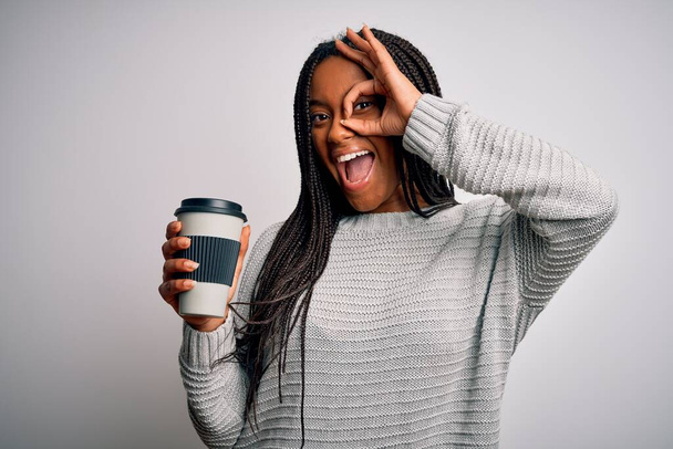 Young african american girl drinking coffe on a take away plastic cup over isolated background with happy face smiling doing ok sign with hand on eye looking through fingers - Fotografie, Obrázek