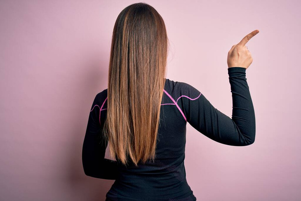 Junge blonde Fitness-Frau in Sportkleidung vor isoliertem Hintergrund posiert rückwärts und zeigt mit der Fingerhand nach vorne - Foto, Bild