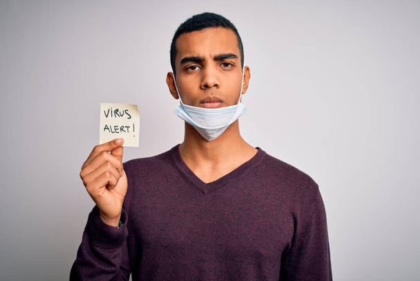 Jeune bel homme afro-américain portant un masque médical tenant alerte au virus rappel avec une expression confiante sur la pensée intelligente du visage grave
 - Photo, image