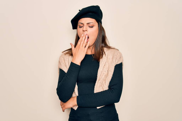 Young beautiful brunette woman wearing casual french beret over white background bored yawning tired covering mouth with hand. Restless and sleepiness. - Fotó, kép