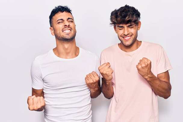 Jeune couple gay portant des vêtements décontractés très heureux et excité faisant geste gagnant avec les bras levés, souriant et criant pour le succès. concept de célébration.  - Photo, image