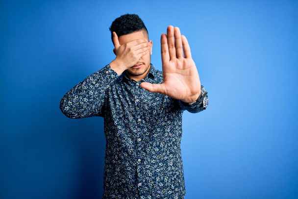 Young handsome man wearing casual shirt standing over isolated blue background covering eyes with hands and doing stop gesture with sad and fear expression. Embarrassed and negative concept. - Photo, Image