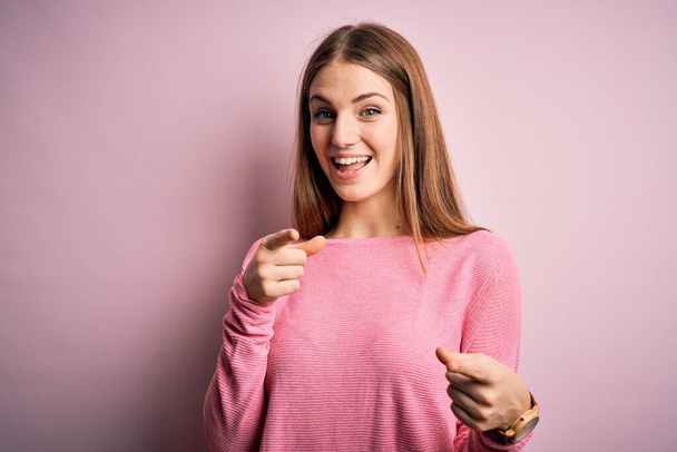 Jonge mooie roodharige vrouw draagt casual trui over geïsoleerde blu achtergrond wijzende vingers naar camera met gelukkig en grappig gezicht. Goede energie en vibraties. - Foto, afbeelding