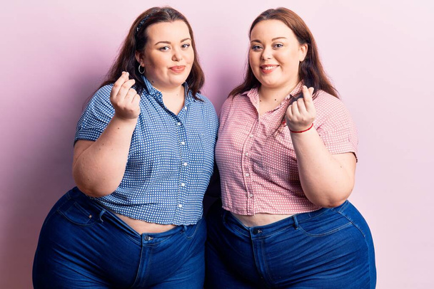 Young plus size twins wearing casual clothes doing money gesture with hands, asking for salary payment, millionaire business  - 写真・画像