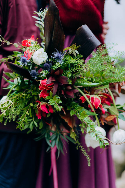 Asymmetric wedding bouquet on a background against the background of a burgundy skirt. - Foto, afbeelding