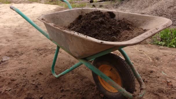 un hombre recoge la tierra con una pala y vierte en el carro de construcción - Metraje, vídeo