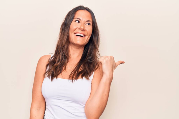Young beautiful brunette woman wearing casual t-shirt standing over isolated white background Smiling happy and positive, thumb up doing excellent and approval sign - Φωτογραφία, εικόνα