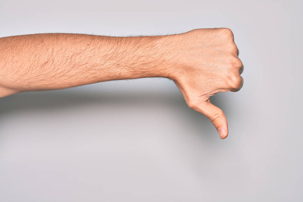 Рука кавказского молодого человека показывает пальцы на изолированном белом фоне, делая большие пальцы вниз жест отказа, неодобрение неприязни и негативный знак - Фото, изображение