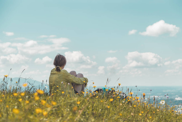 Deportiva chica en un viaje de senderismo está sentado en el prado y disfrutar de la vista sobre la lejana ciudad
 - Foto, Imagen