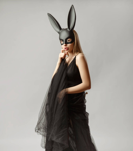 Beautiful blonde in a rabbit mask in a sexy evening dress on a white background - Fotó, kép