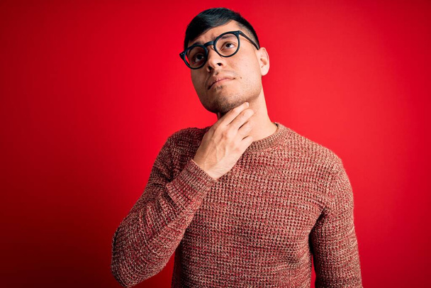 Jovem hispânico bonito vestindo óculos nerd sobre fundo vermelho Tocando pescoço doloroso, dor de garganta para gripe, cravo e infecção
 - Foto, Imagem