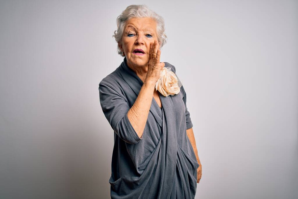 Senior hermosa mujer de pelo gris con vestido casual de pie sobre fondo blanco mano en boca diciendo rumor secreto, susurrando conversación maliciosa
 - Foto, Imagen