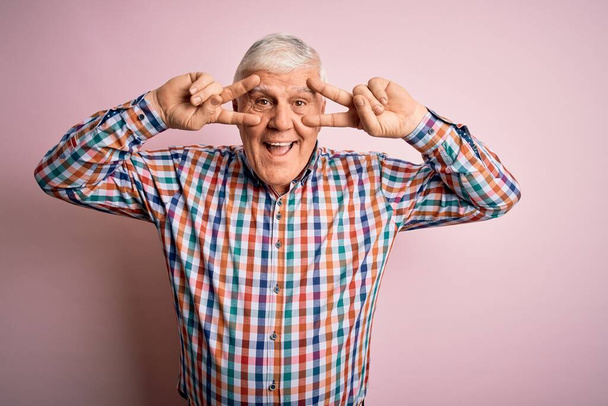 Senior handsome hoary man wearing casual colorful shirt over isolated pink background Doing peace symbol with fingers over face, smiling cheerful showing victory - Fotoğraf, Görsel