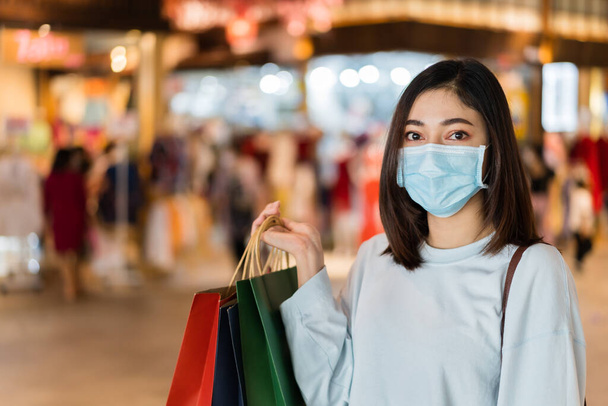 young woman shopping with bag at mall and her wearing medical mask for prevention from coronavirus (Covid-19) pandemic. new normal concepts - Photo, image