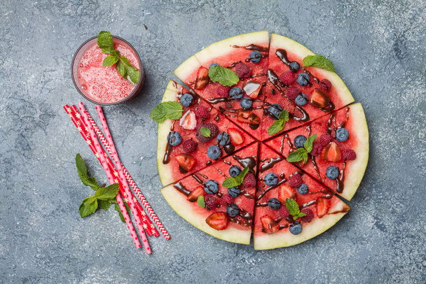 kleurrijke tropische fruit watermeloen pizza belegd met bessen en chocolade saus met watermeloen sap over grijze steen achtergrond, bovenaanzicht - Foto, afbeelding